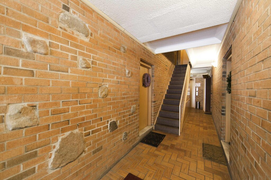 Ground floor hallway at 26 Oliver Street with brick walls, a parquet floor, the stairs and the elevator.