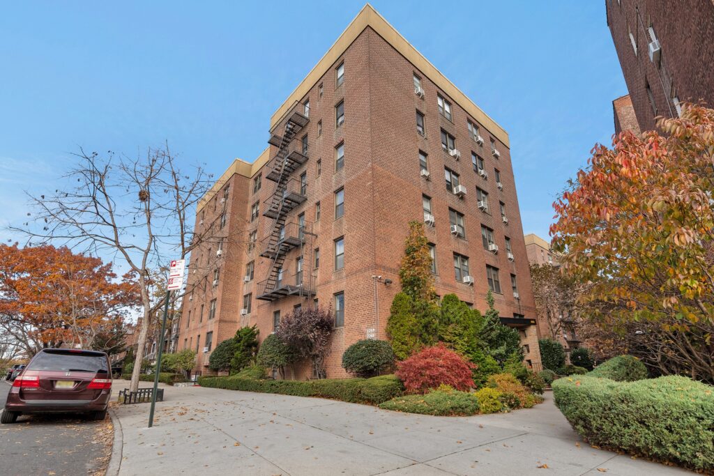 Exterior of the 1955 red brick co-op at 7259 and 7261 Shore Road in Bay Ridge, Brooklyn, a six story elevator building with landscaping at the entrance.