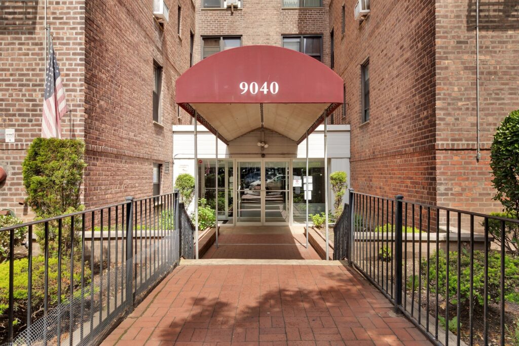 Entrance of 9040 Fort Hamilton Parkway in Bay Ridge, Brooklyn, with a red awning over the lobby doors and a brick walkway.